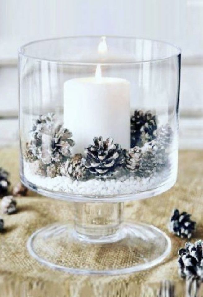 a candle in a glass bowl filled with snow and pine cones