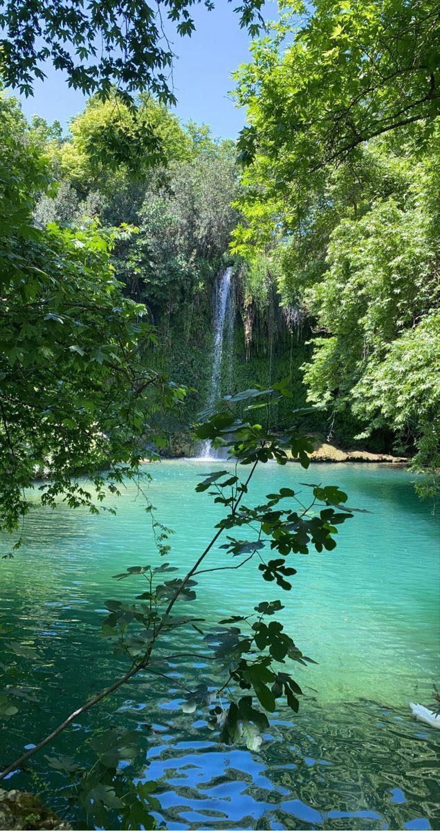 there is a waterfall in the middle of this lake with blue water and green trees