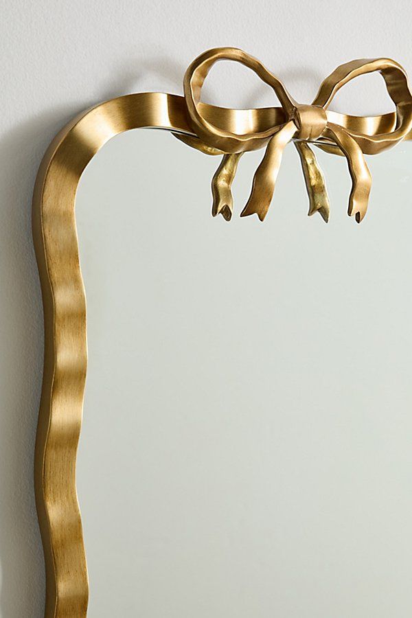 a mirror with a gold bow hanging on it's side next to a wall