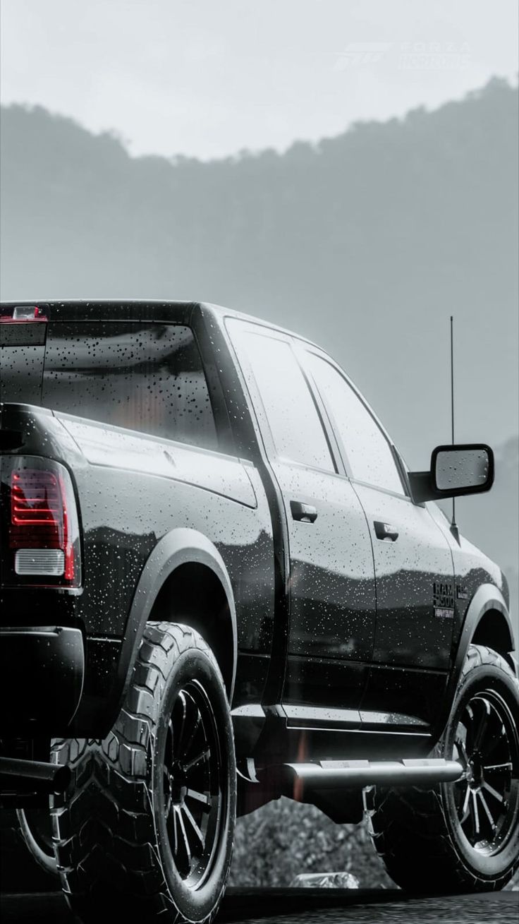 a black and white photo of a truck with snow on the tires, in front of mountains