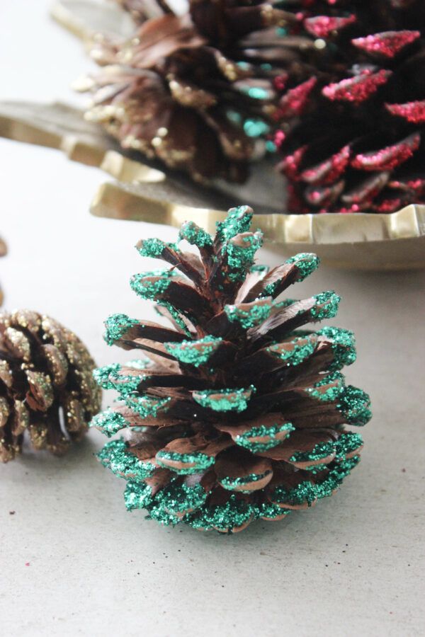 two pine cones are sitting next to each other on the table, one has green and red glitter