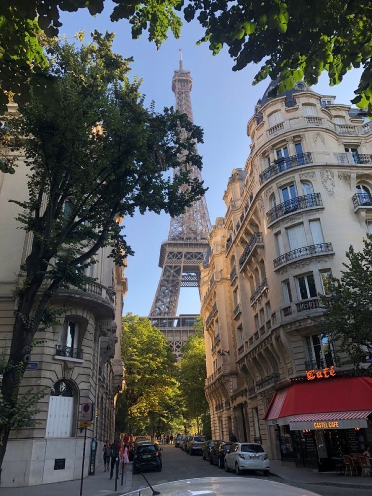 the eiffel tower is seen through trees in this street view from across the street