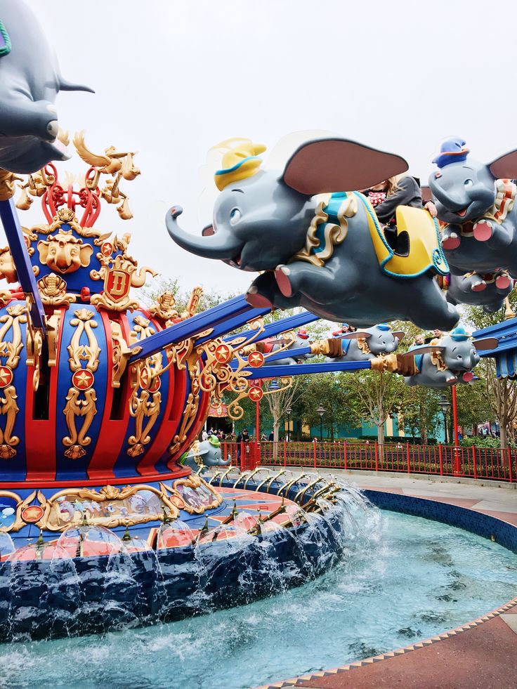 an amusement park with elephants and mice on top of the water fountain in front of them