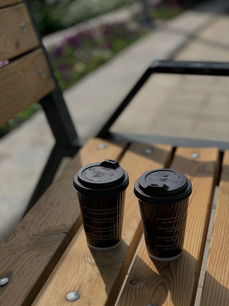 two black coffee cups sitting on top of a wooden bench next to eachother