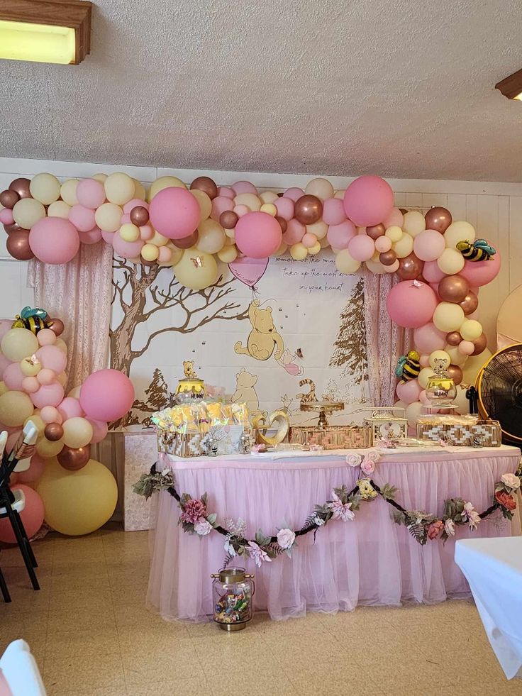 a table with pink and gold balloons on the wall next to a white table cloth draped over it