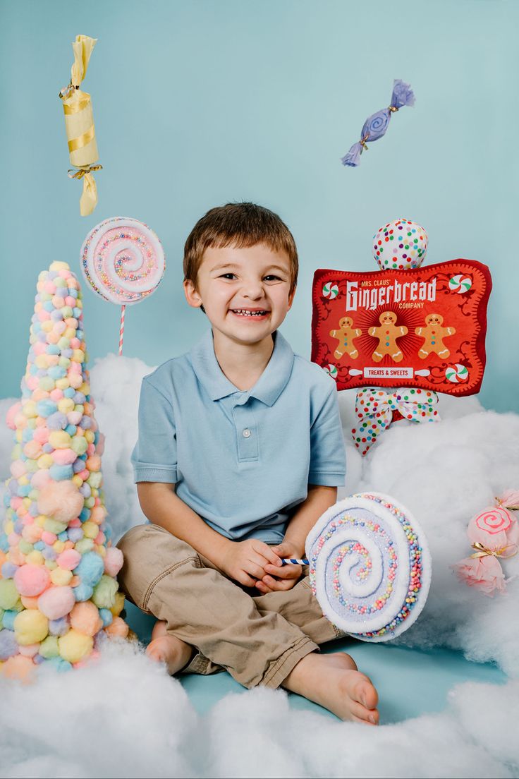 a young boy sitting in front of a cake and candy display with an assortment of candies