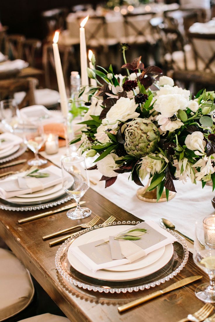 the table is set with white and black flowers, silverware, candles and napkins