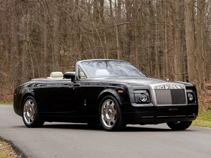 a black rolls royce parked on the side of a road in front of some trees