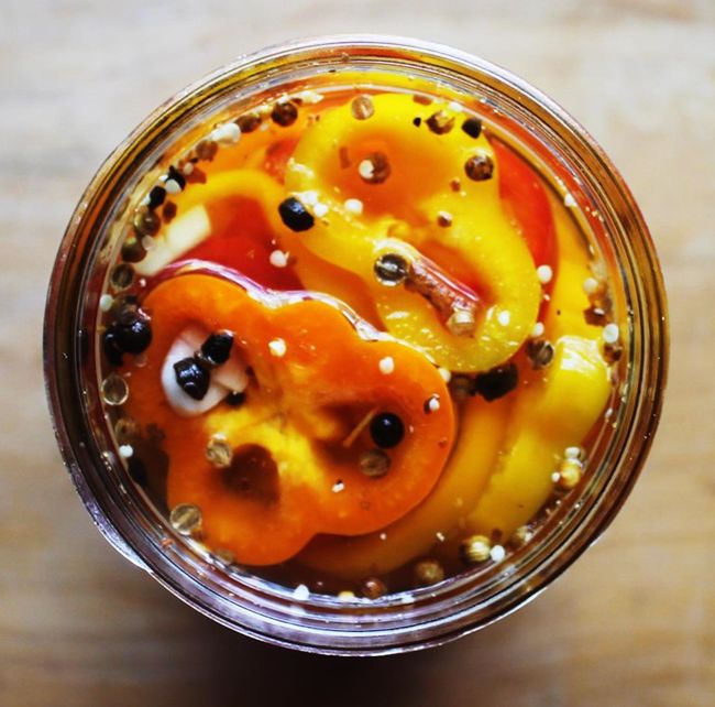 a jar filled with different colored peppers on top of a wooden table