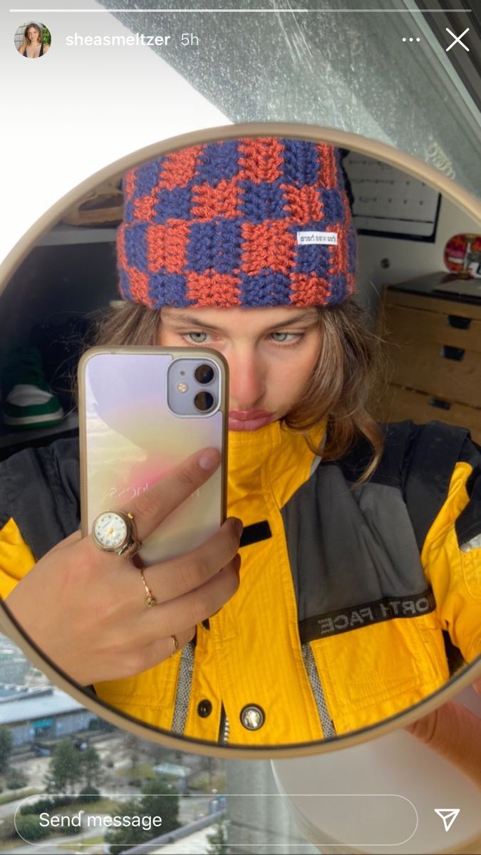 a woman taking a selfie in the mirror with her cell phone and wearing a hat