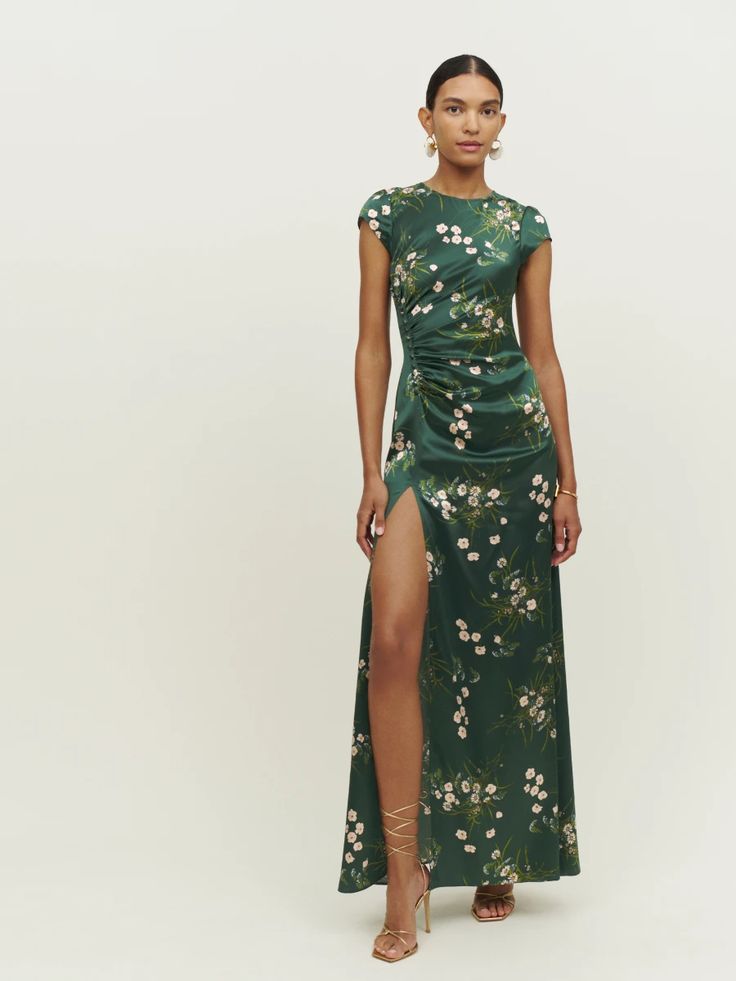 a woman wearing a green dress with white flowers on it and a slit down skirt