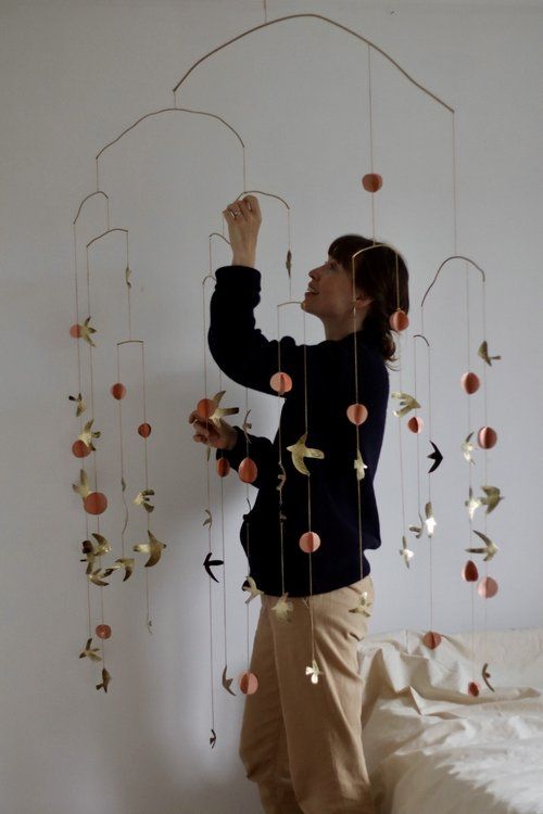 a woman standing in front of a mobile made out of paper circles and leaves, with her hands up to the ceiling