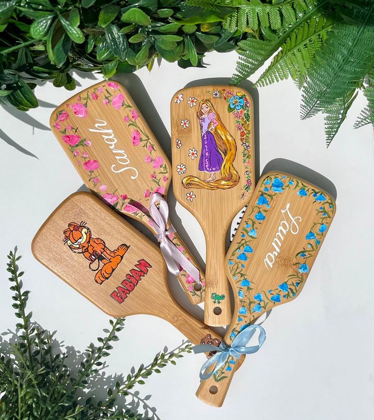 four wooden paddles with disney characters on them are sitting next to some green plants