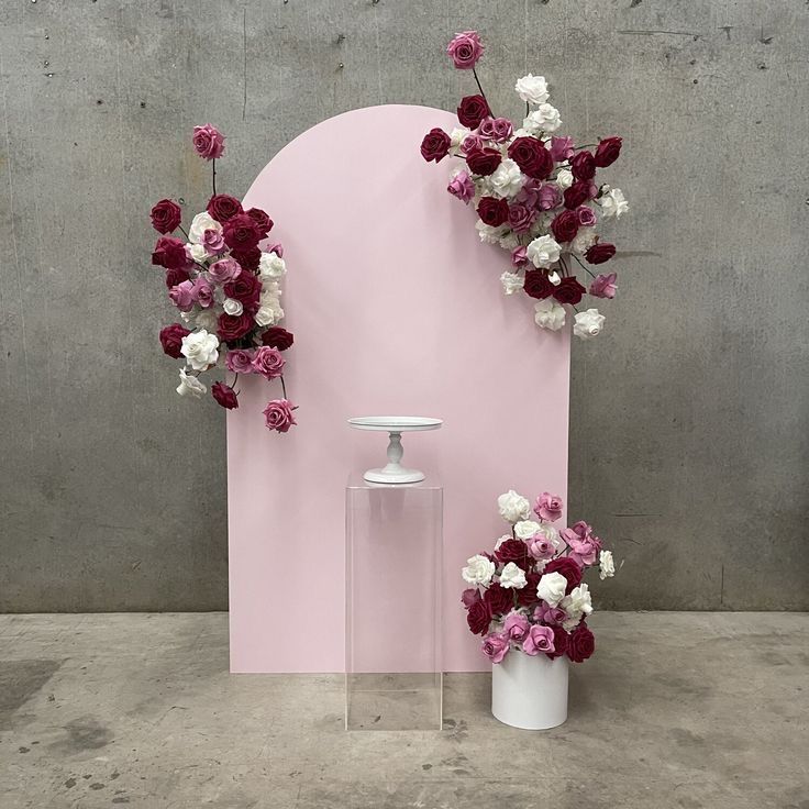 two vases with flowers in front of a pink wall and a white vase on the floor