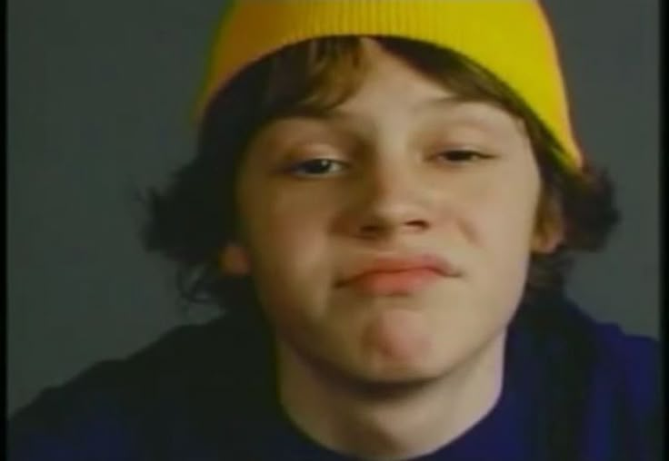 a young man wearing a yellow hat and looking at the camera