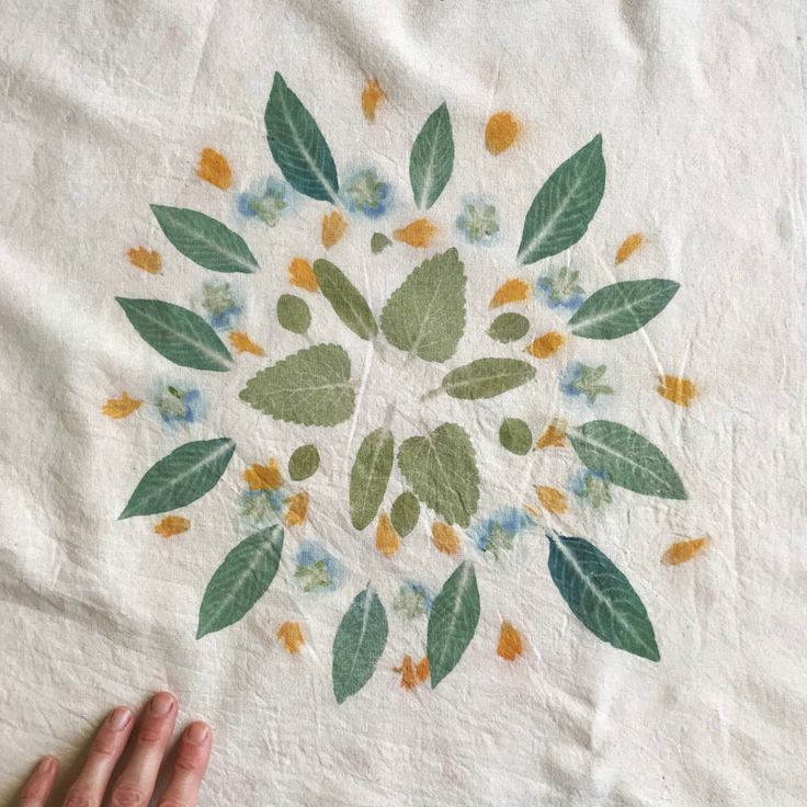 a person's hand is holding onto a white table cloth with leaves and flowers on it