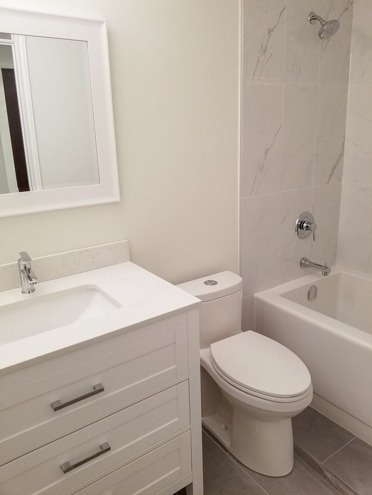 a white bathroom with a toilet, sink and bathtub next to a mirror on the wall