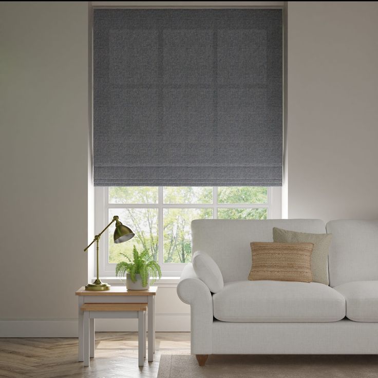 a white couch sitting under a window next to a table with a lamp on it