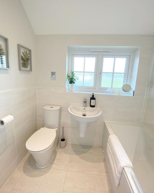 a white bathroom with a sink, toilet and bathtub next to a large window