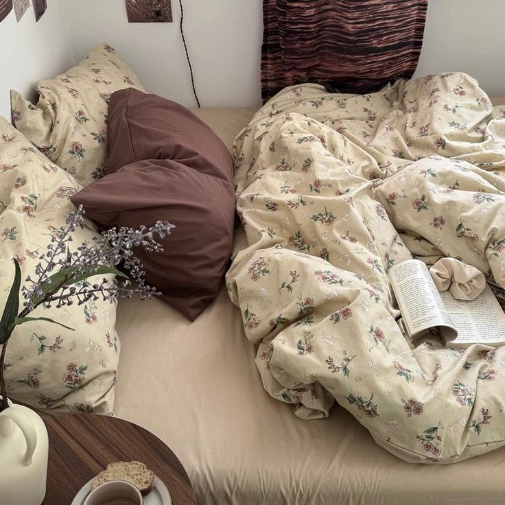 an unmade bed covered in blankets and pillows with a book on the end table