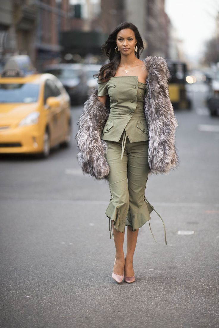 a woman walking down the street wearing a green outfit with fur stoler and heels