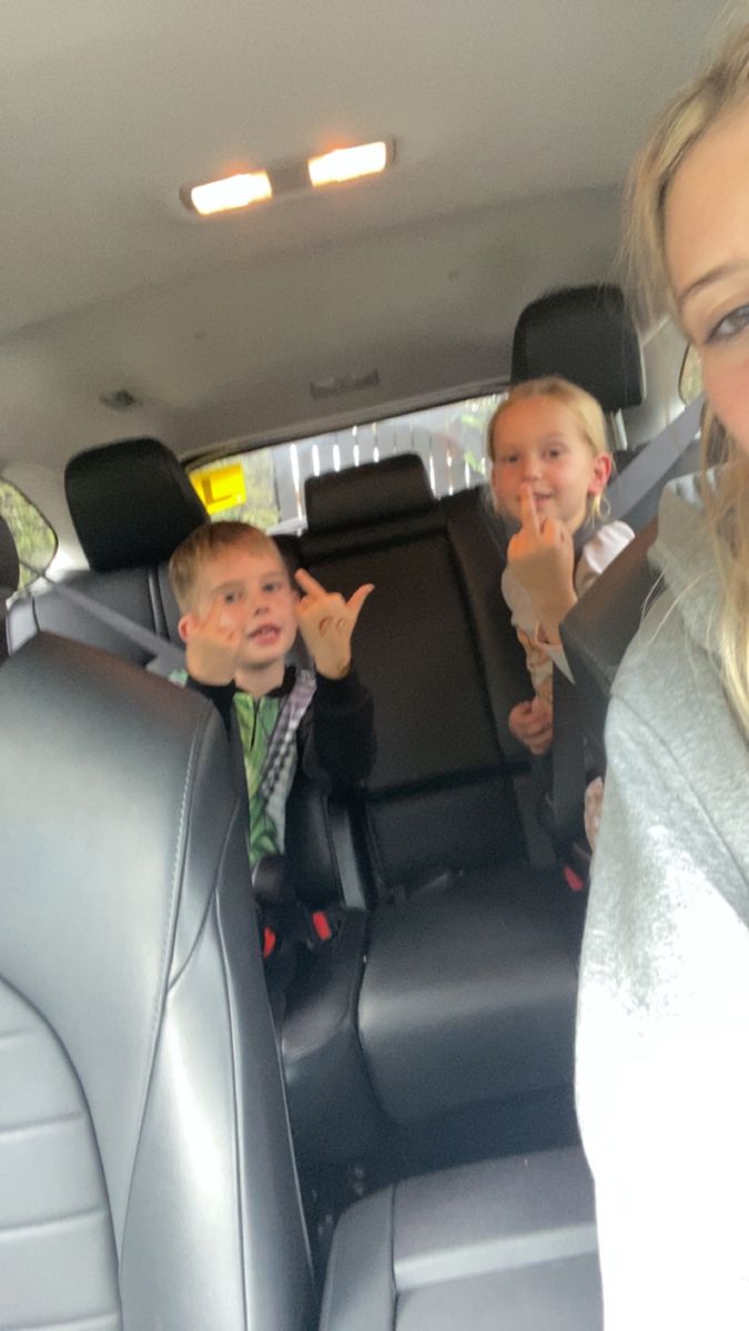 two children sitting in the back seat of a car with their hands up and smiling