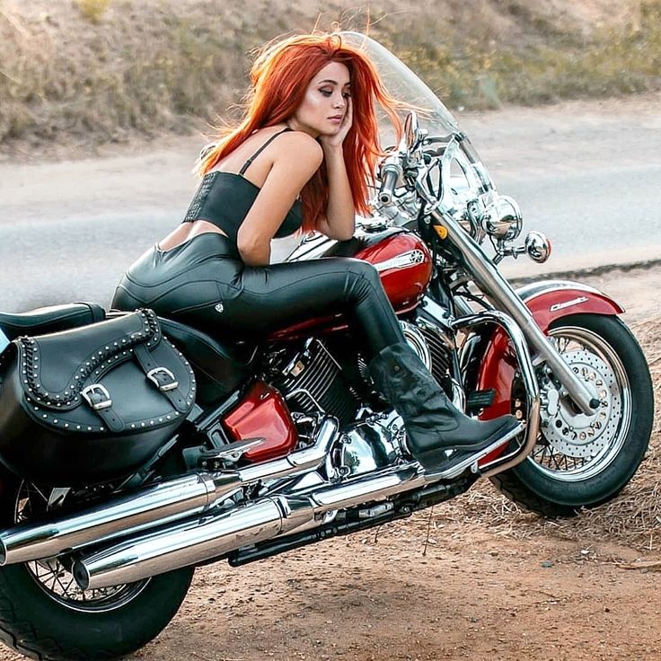 a woman sitting on top of a red motorcycle in the middle of a dirt road