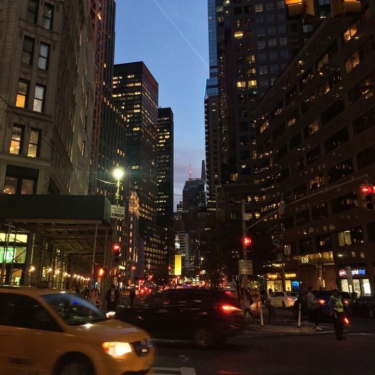 a city street filled with lots of tall buildings at night, traffic lights and people