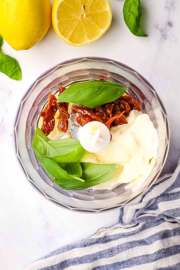 a glass bowl filled with food next to lemons and other ingredients on a white table