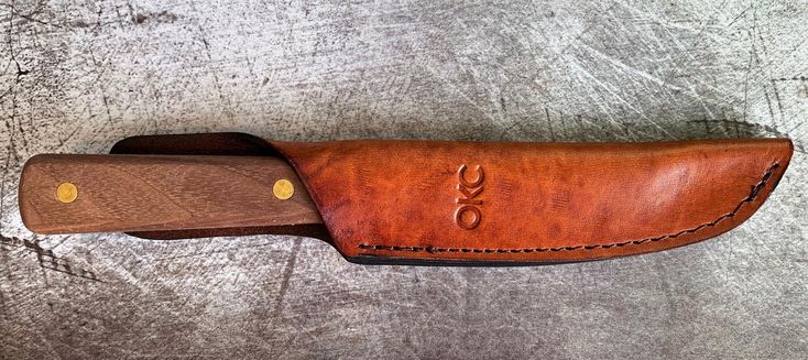 a knife with a brown leather sheath on it's side, resting on a gray surface