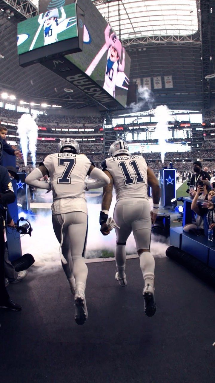 two football players run onto the field in front of an onlooker at a sporting event