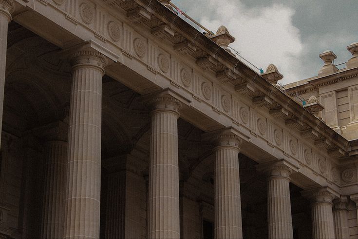 an old building with columns and a clock on the top, under a cloudy sky