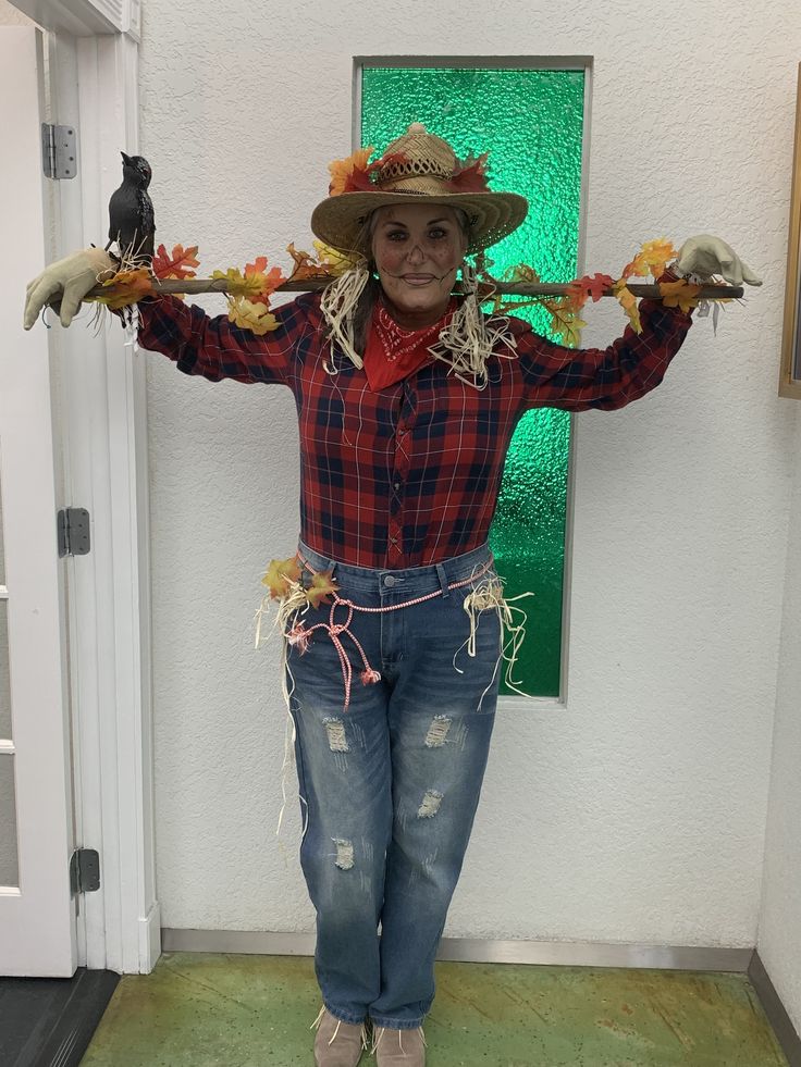 a woman wearing a scarecrow hat and holding two birds on her arms, standing in front of a door