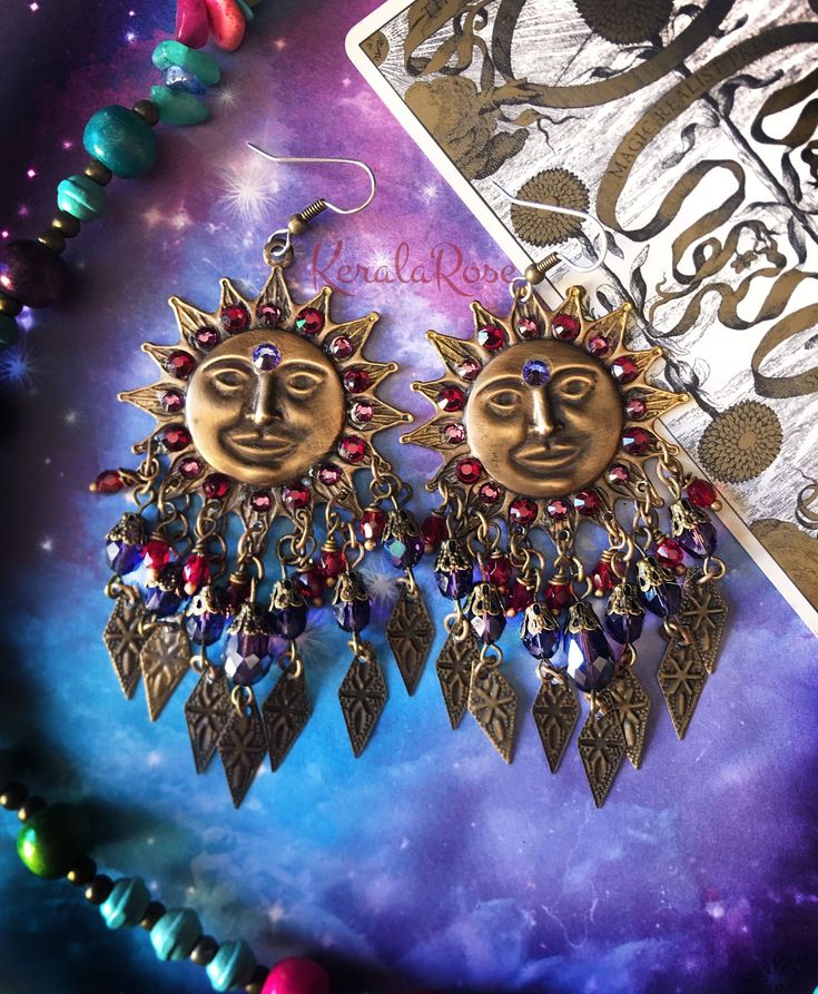 'Make some time for the sunshine!'  These Celestial Boho Chandelier Earrings are made with large hand-antiqued brass Sun stampings richly decorated with crystal rhinestone 3'rd eyes and rays.  Amethyst & Garnet Red crystal, glass beads and metal diamond  charms add to the whimsical design.  Available in Posts, Clip-Ons or French Wires. -3 1/4" Long(not including piercing) x 1 3/4" Wide -0.3 oz. ea. *Comes Ready To Gift in Decorative Packaging *Each Pair is Made Just for You!  Kerala Rose Pintere Bohemian Summer Jewelry With Sun And Moon Design, Bohemian Sun And Moon Design Jewelry For Summer, Bohemian Sun Design Adjustable Earrings, Bohemian Sun And Moon Earrings For Festivals, Bohemian Dangle Earrings With Sun Design, Bohemian Sun And Moon Design Earrings For Festival, Bohemian Sun Design Dangle Earrings, Bohemian Sun Design Earrings For Festival, Multicolor Jeweled Bohemian Earrings