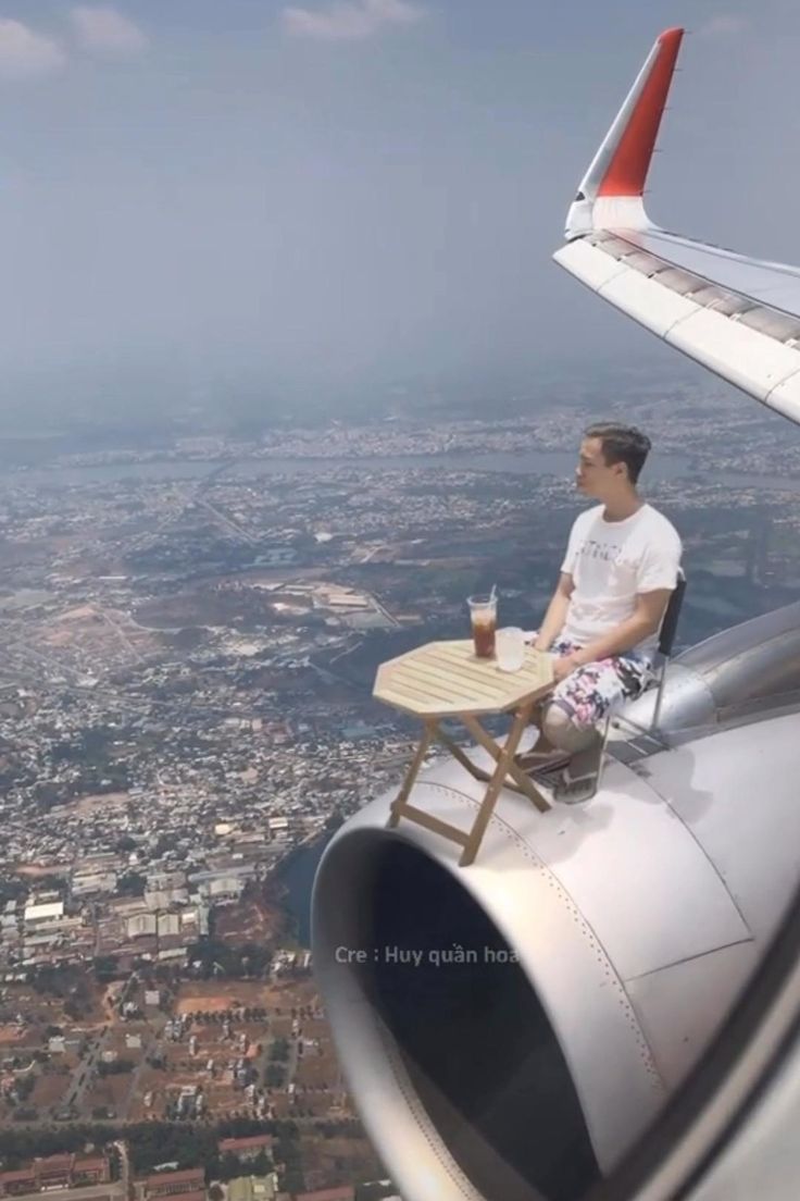 a man sitting at a table on the wing of an airplane looking out over a city