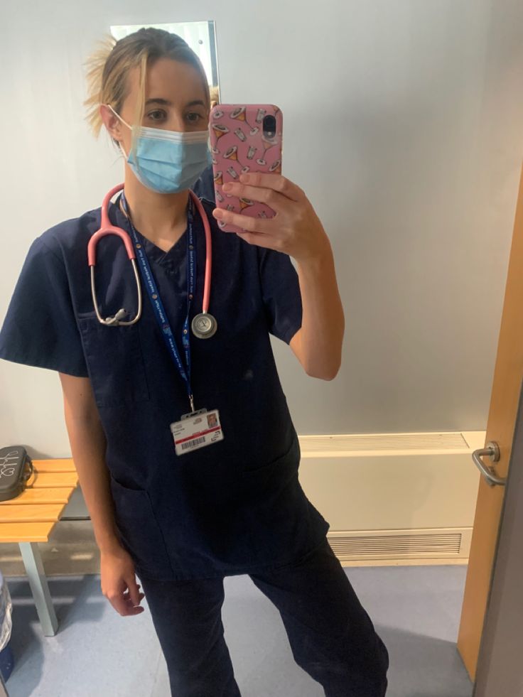 a woman in scrubs is taking a selfie with her cell phone and wearing a face mask