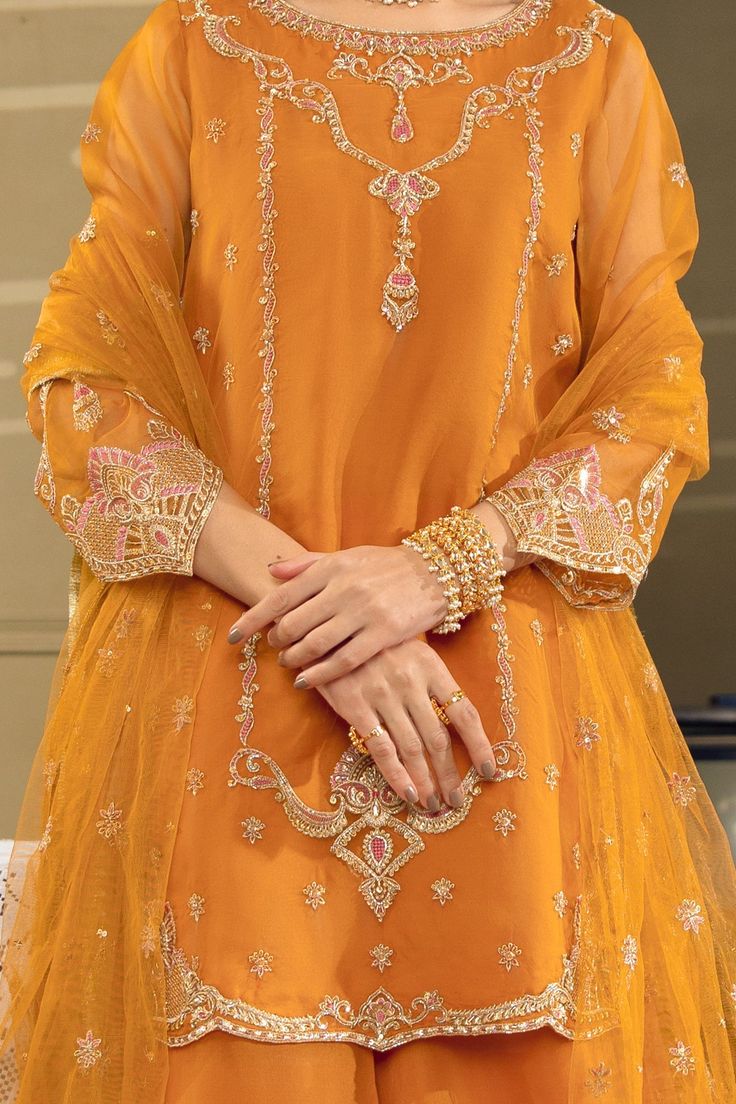 Mustard Orange Embroidered Pakistani Kameez Sharara Party Dress exemplifies exclusive cutwork, embellishments and superior details on lustrous draperies for your approaching festive season wardrobe. Embroidered Kameez: The traditional dress has a very stylish and elegant neckline emblazoned with golden threadwork. This elegant attire is embellished with floral designs on Silk Tissue and adorned with pearls, dabka, naqshi, and gleaming stones. Sharara: Pakistani Sharara with traditional gold work Pakistani Kameez, Mustard Orange, Latest Bridal Dresses, Pakistani Fancy Dresses, Pakistani Dresses Casual, Pakistani Fashion Party Wear, Beautiful Pakistani Dresses, Dress Design Patterns, Simple Pakistani Dresses