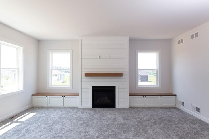 an empty living room with two windows and a fire place in the middle of it