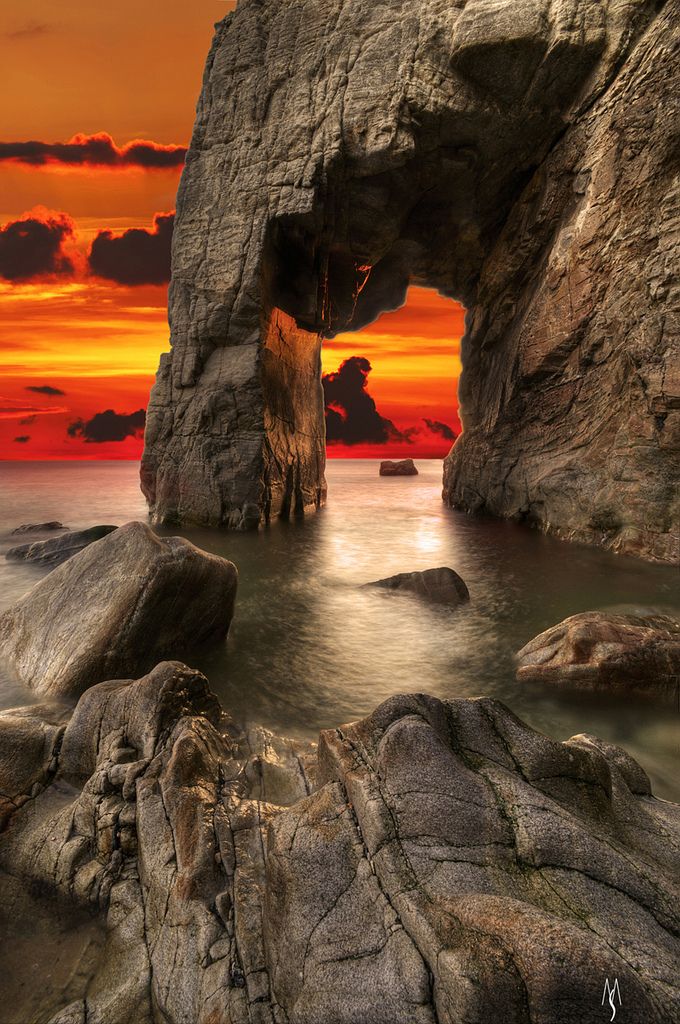 the sun is setting over an ocean with rocks and water in front of it, as well as a large rock formation