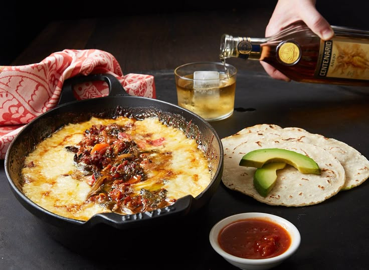 two black bowls filled with food on top of a wooden table next to a cup