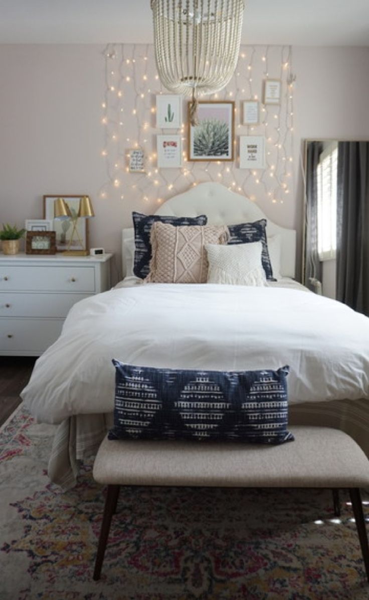 a white bed sitting under a chandelier next to a window covered in lights