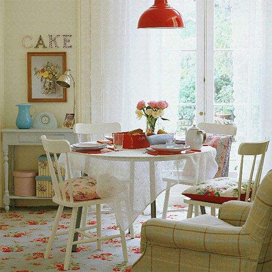 a dining room table and chairs with flowers on the rug in front of it, next to a window