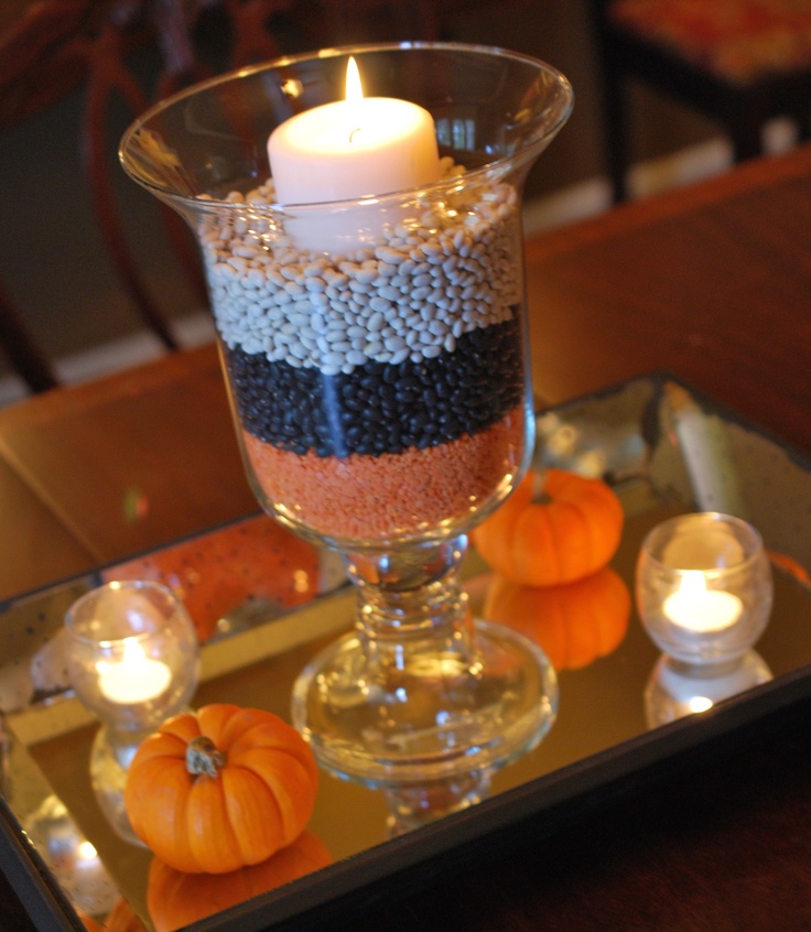 a candle is lit in a glass vase filled with beads and pumpkins on a tray