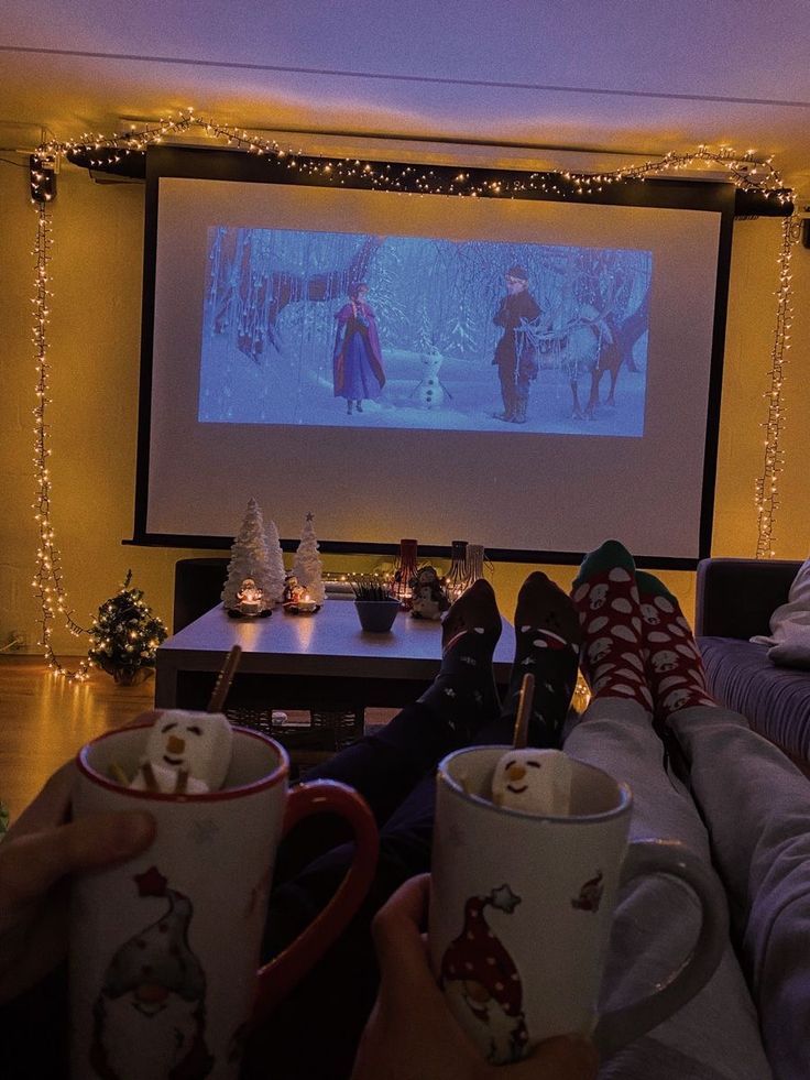 two people sitting in front of a projection screen holding coffee mugs with christmas decorations on them