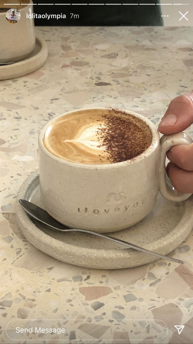 a person holding a cup of coffee on top of a saucer with a spoon