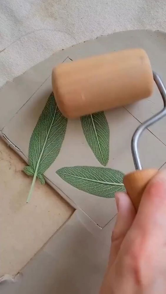 a person using a rolling pin to paint leaves on a piece of paper with glue