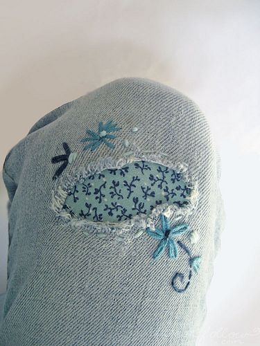 a blue hat with embroidered flowers and birds on it's side, sitting on a white surface