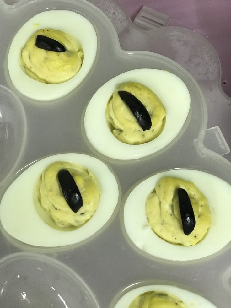 several deviled eggs with black condiments in an egg tray