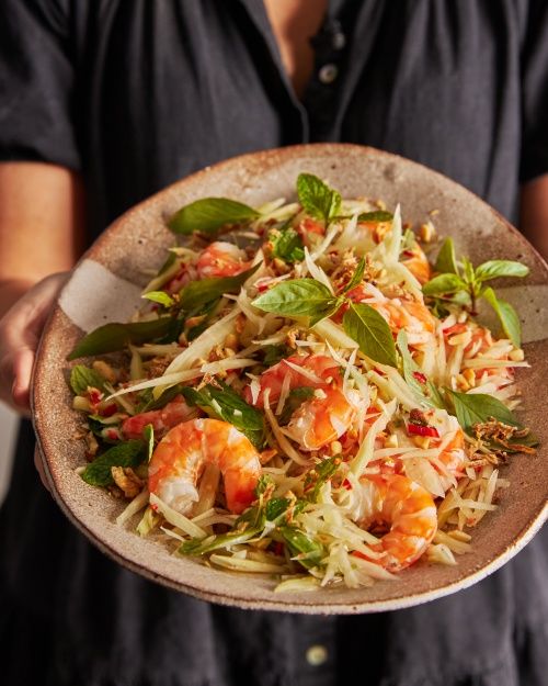 a person holding a plate full of food with shrimp and lettuce on it