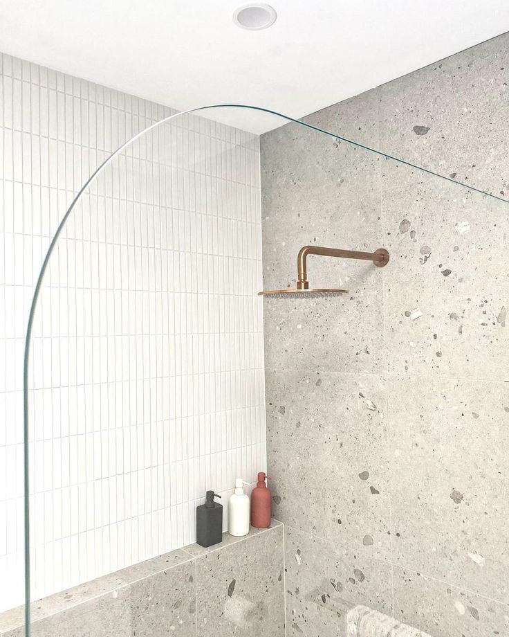 a bathroom with a glass shower head and white tile walls, along with toiletries